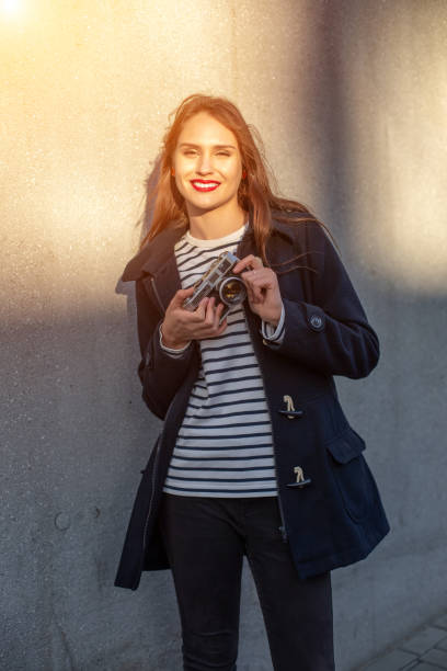 photographe féminin souriant dans la veste restant devant le mur prêt à faire la nouvelle photo. fusée de soleil - concrete wall flash photos et images de collection