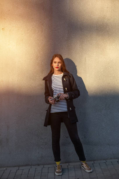 photographe féminin souriant dans la veste restant devant le mur prêt à faire la nouvelle photo. fusée de soleil - concrete wall flash photos et images de collection