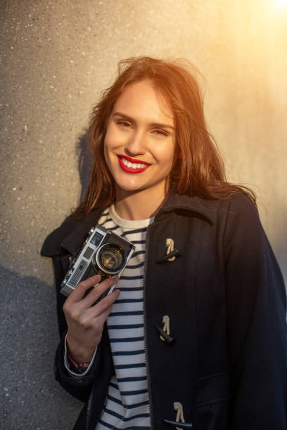 photographe féminin souriant dans la veste restant devant le mur prêt à faire la nouvelle photo. fusée de soleil - concrete wall flash photos et images de collection