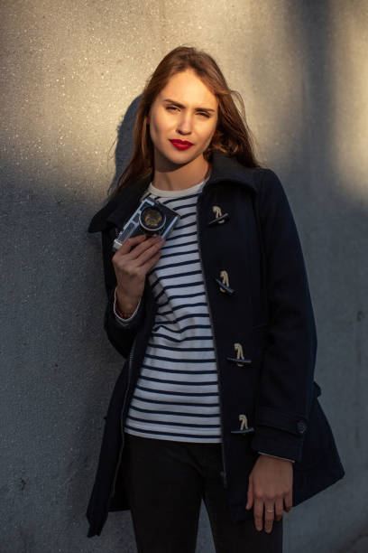 photographe féminin souriant dans la veste restant devant le mur prêt à faire la nouvelle photo. fusée de soleil - concrete wall flash photos et images de collection