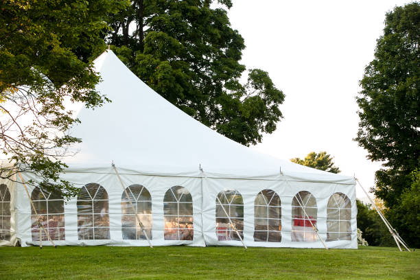 木に囲まれた芝生の上に、側面を下にして設置される白い結婚式のテント - テント 写真 ストックフォトと画像