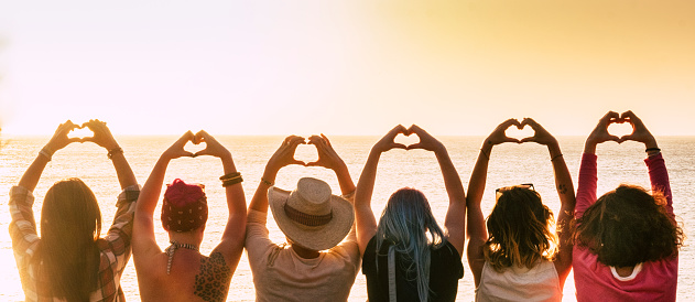 Group of diversity alternative young woman enjoying the sunset at the sea doing hearth symbol with hands - people enjoying friendly lifestyle - vacation in friendship concept for females