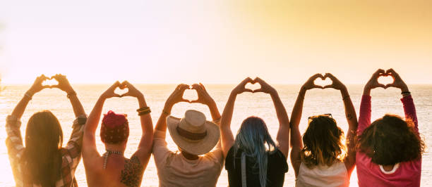 多樣性的小組另類年輕女子享受日落在海上做爐邊的標誌與手-人享受友好的生活方式-假期在友誼概念為女性 - 情人節 節日 圖片 個照片及圖片檔