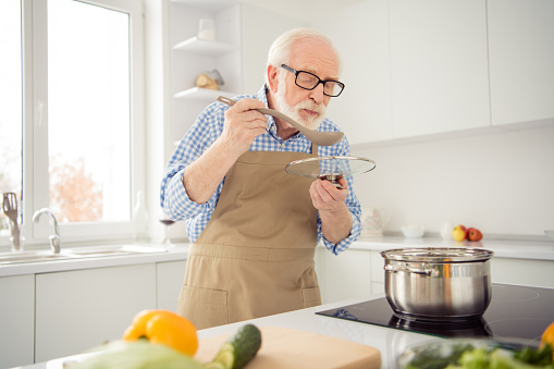 Close up photo grey haired he his him grandpa appetite waiting guests cooking favorite family dish trying taste wait ready wear specs casual checkered plaid shirt jeans denim outfit kitchen indoors