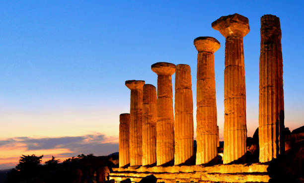 colonne in rovina del tempio di eracle nella famosa antica valle dei templi al tramonto dell'ora blu nella sera d'estate, agrigento, sicilia, italia. patrimonio mondiale dell'unesco. - temple of heracles foto e immagini stock