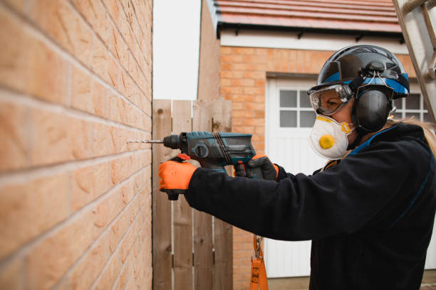 Drilling onto the Wall Side view of a female blue collar worker standing outdoors in her protective clothing. She is using a power drill as she drills a hole into the side of the house. helmet hardhat protective glove safety stock pictures, royalty-free photos & images