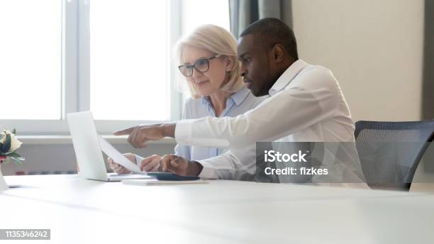 African American Employee Pointing At Laptop Discussing Paperwork With Colleague Stock Photo - Download Image Now