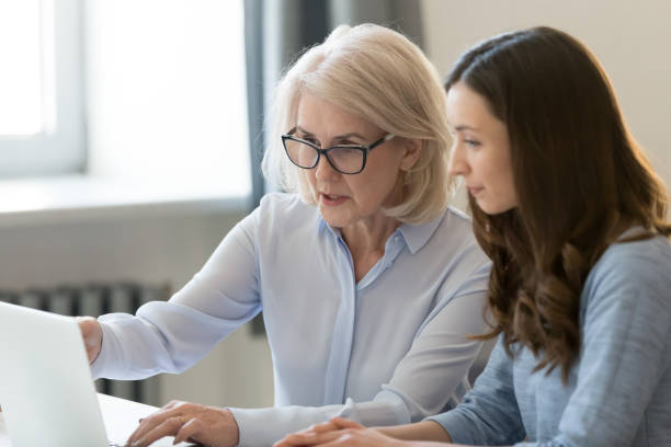 serio vecchio mentore insegnante stagista o studente che punta al laptop - coach foto e immagini stock