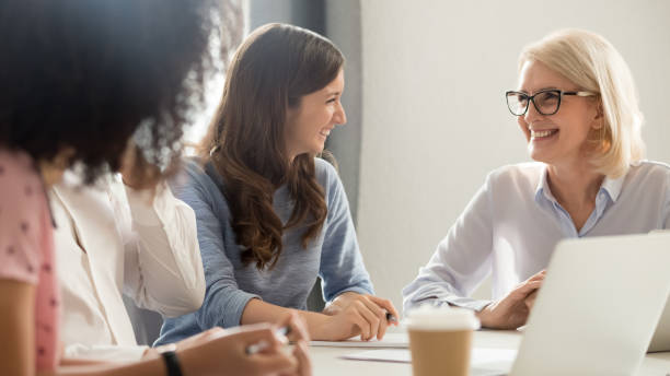 przyjacielskie uśmiechnięte stare i młode biznesmenki rozmawiają śmiejące się na spotkaniu - leadership business women senior adult zdjęcia i obrazy z banku zdjęć