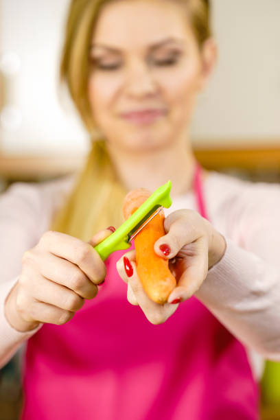 Woman peeling vegetables using food peeler. Cooking female preparing carrot before serving.