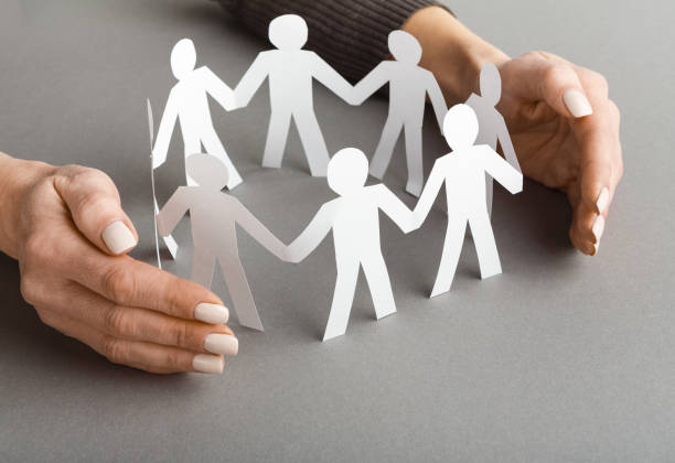 istock Businessperson's hand protecting paper cut out figures 1135348952
