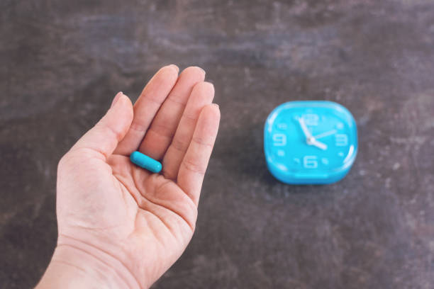 istock Time to using the Pill. Bright blue capsule pill in women hand on alarm clock background. Female hands holding one capsule 1135349294