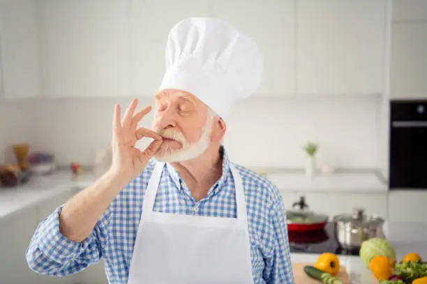 Close up photo grey haired he his him grandpa arms hands fingers okey symbol belissimo tasting smelling eyes closed wear baker chefs costume casual checkered plaid shirt jeans denim outfit kitchen