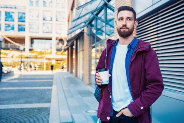 istock Handsome young man in purple winter jacket drinking coffee. The guy drinking coffee on the street. 1135351989