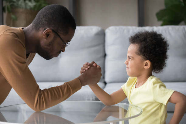 istock African dad and kid son with funny angry faces armwrestling 1135353576