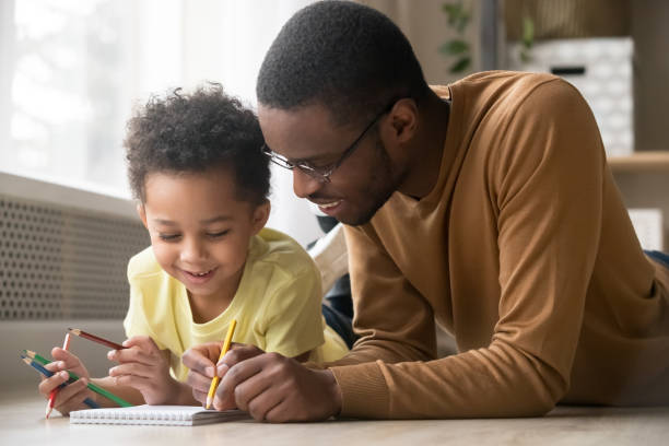 afrikanischer papa und kleiner kleintoddgänger sohn zeichnen mit buntstiften - preschool father offspring child stock-fotos und bilder