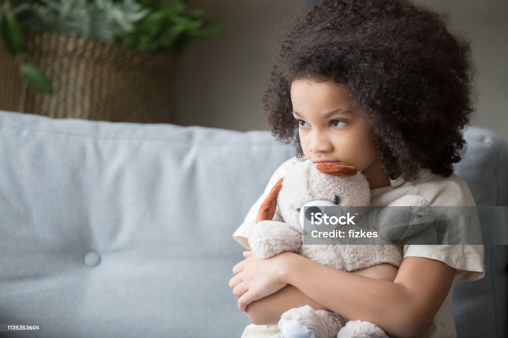 Upset lonely african kid girl holding teddy bear looking away Upset lonely bullied little african american kid girl holding teddy bear looking away feels abandoned abused, sad alone preschool mixed race child orphan hugging stuffed toy, charity adoption concept Child Stock Photo