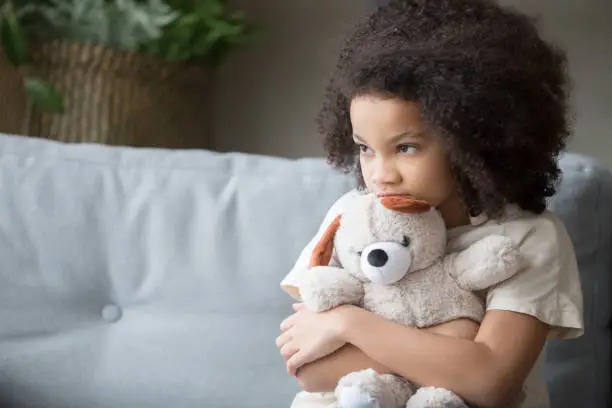 Upset lonely bullied little african american kid girl holding teddy bear looking away feels abandoned abused, sad alone preschool mixed race child orphan hugging stuffed toy, charity adoption concept