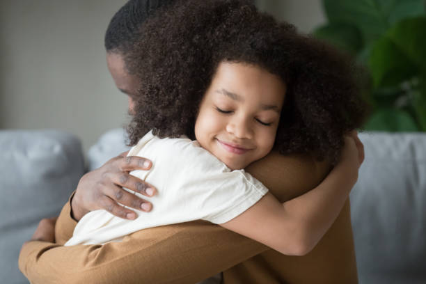 Cute mixed race child daughter embracing father feeling love connection Cute funny mixed race child daughter embracing black father holding tight feeling love connection affection concept, happy african family dad and little kid girl hugging cuddling bonding at home foster care stock pictures, royalty-free photos & images