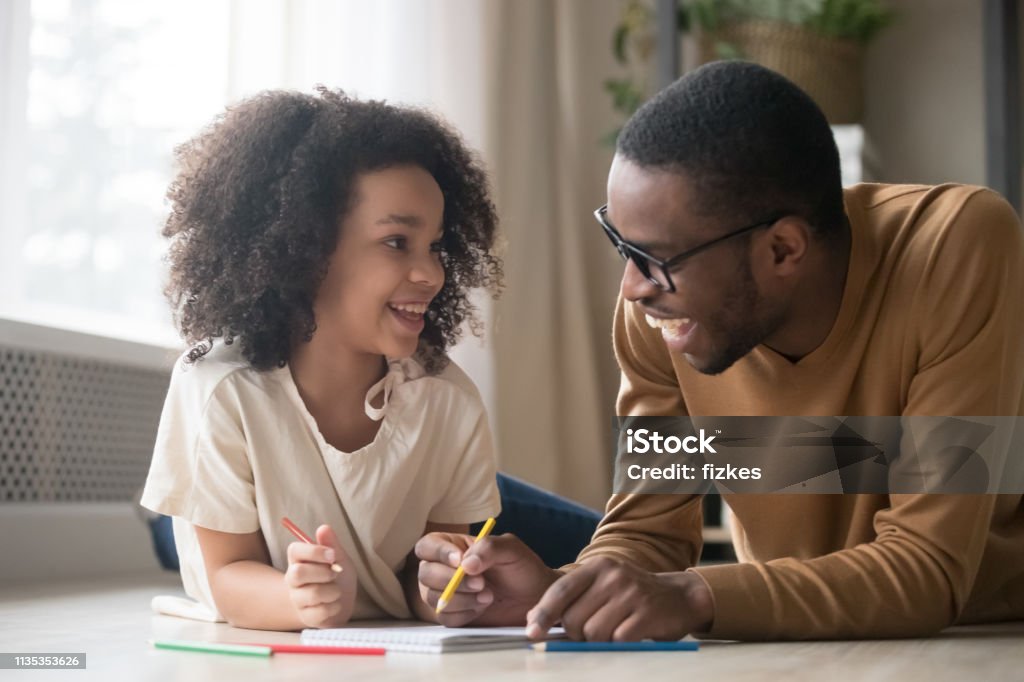 Desenho Africano da menina da criança com os lápis que têm o divertimento com paizinho - Foto de stock de Criança royalty-free