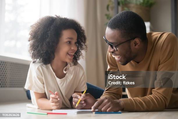 Foto de Desenho Africano Da Menina Da Criança Com Os Lápis Que Têm O Divertimento Com Paizinho e mais fotos de stock de Criança