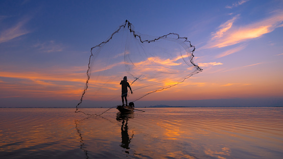 Silhouette Fisherman fishing nets on the boat. Silhouette of fishermen using coop-like trap catching fish in lake with beautiful scenery of nature morning sunrise.