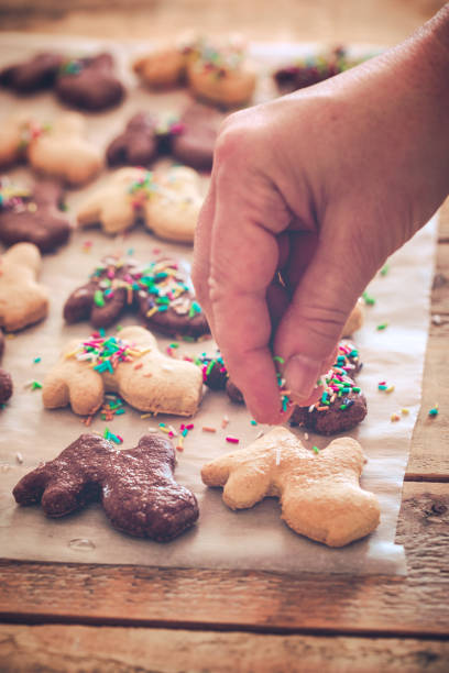 Fresh made Easter bunny cookies at baking paper sheet being decorated with cookie sprinkles, close-up