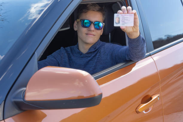 szczęśliwy nastolatek pokazuje swoje prawo jazdy z otwartego okna samochodu. koncepcja szkoły jazdy - learning to drive zdjęcia i obrazy z banku zdjęć