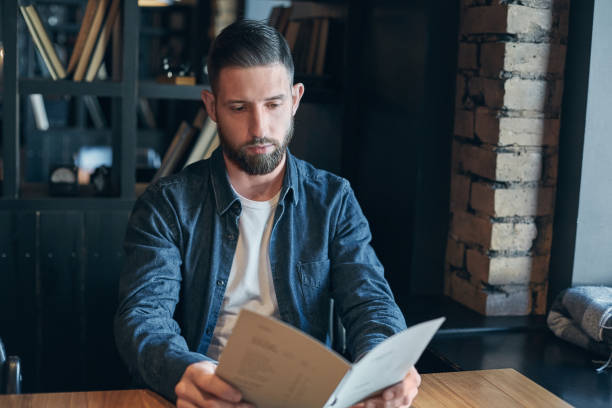 istock Young man sitting in a cafe at the table and watching the menu to make an order 1135358158
