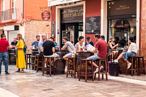 Malaga, Spain - August 28, 2018.  Tourists drinking and eating on a terrace at a Mitjana taverna from Malaga historic center, Spain