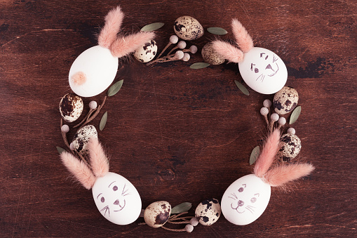 Happy Easter wreath! Spring holidays, tradition, advertisement concept. Flat lay of white Easter eggs with bunny ears on wooden desk, top view