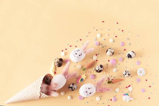 Top view and flat lay of conceptual arrangement decoration for Happy Easter holiday on yellow background. Colorful pastel eggs and topping spill out of the waffle horn with copy space.