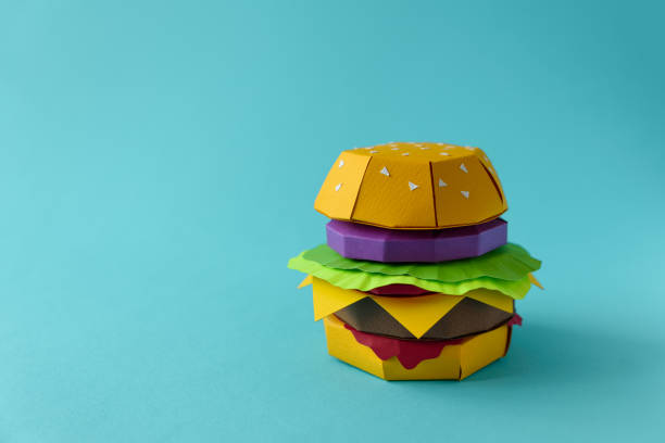 istock Paper cheeseburger with beef, cheese, tomato, lettuce, onion and sauce on a blue background. Copy space. Creative or art food concept 1135368924
