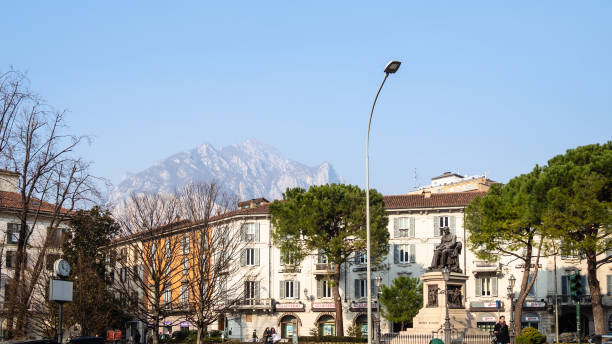 Lecco, Italy - February 20, 2019: people on square piazza Manzoni with Monument Alessandro Manzoni in Lecco city in evening. Lecco is city in Lombardy, the capital of the province of Lecco
