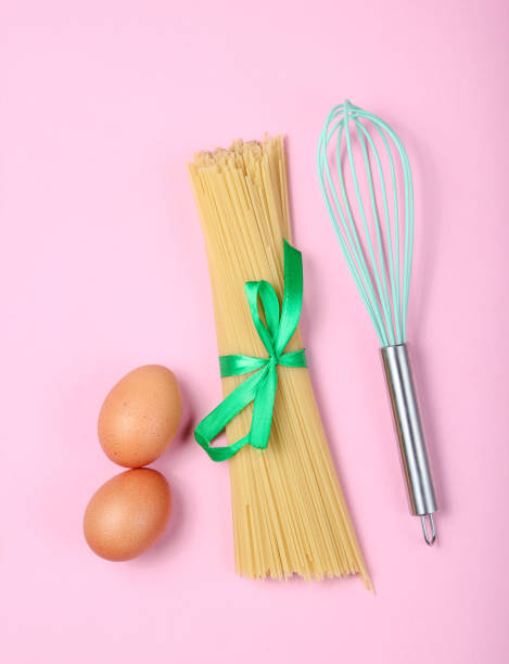 istock Culinary concept, cooking process. Pasta, chicken eggs, whisk on pink background. Top view, flat lay style 1135377449