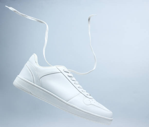 One white unisex sneaker and floating laces on gray background, minimalism