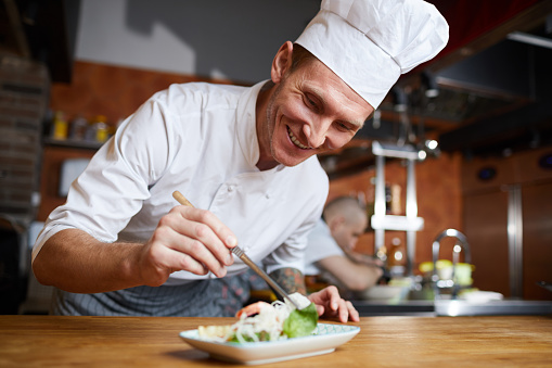 Portrait of professional chef plating Asian seafood dish in restaurant, copy space