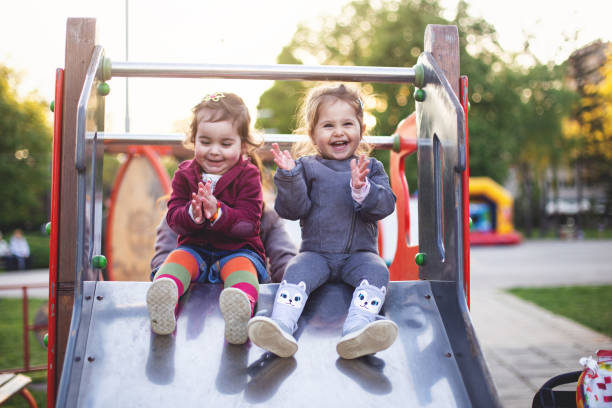 Cheerful little girls sitting on a slide at the playground Cute little toddler sister enjoying the easter egg hunt in the park. toddlers playing stock pictures, royalty-free photos & images