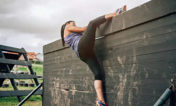 Female participant in an obstacle course climbing a wall