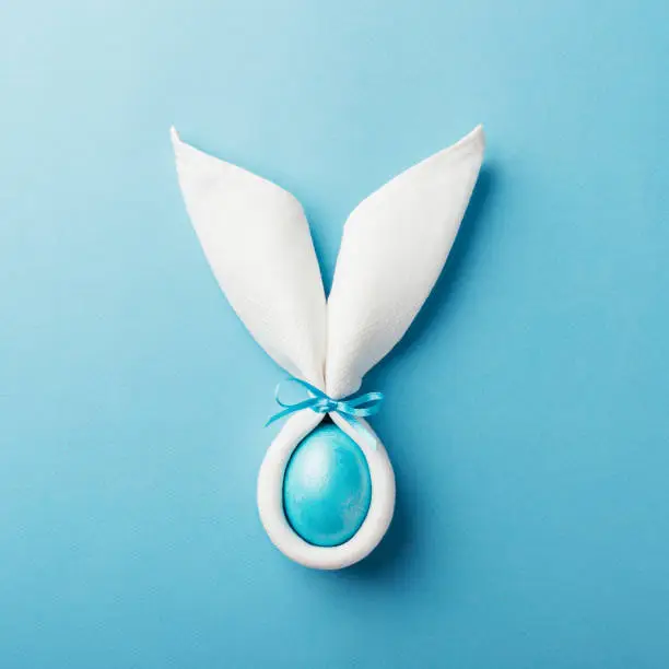 Photo of Easter bunny ears with egg on blue background.