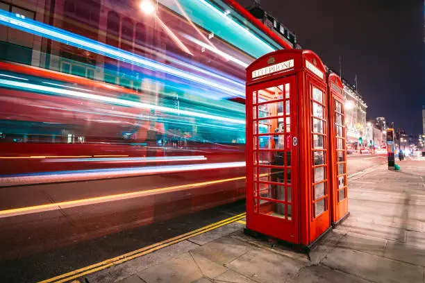 Photo of Light trails of a double decker bus next to the iconic telephone booth in London