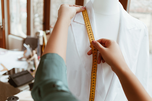 The main thing is right size. Woman designer is measuring white shirt with tape, close-up