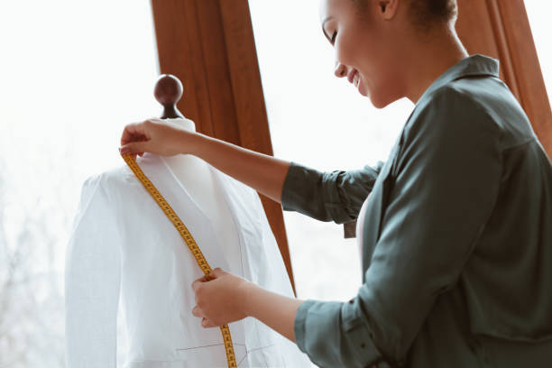 istock Young designer with tape is measuring white shirt. Side view 1135397128