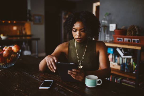 Young woman having a coffee in her apartment while browsing the web on tablet