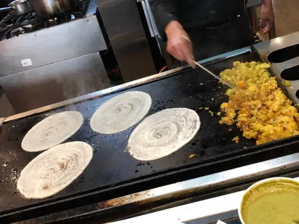 Photo of Image of hotel restaurant chef making savoury Indian dosas pancakes / crepes on kitchen hot plate photo