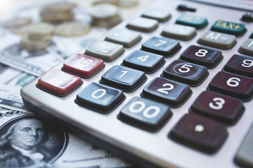 Calculator with dollars and coins on wooden background. Close up.