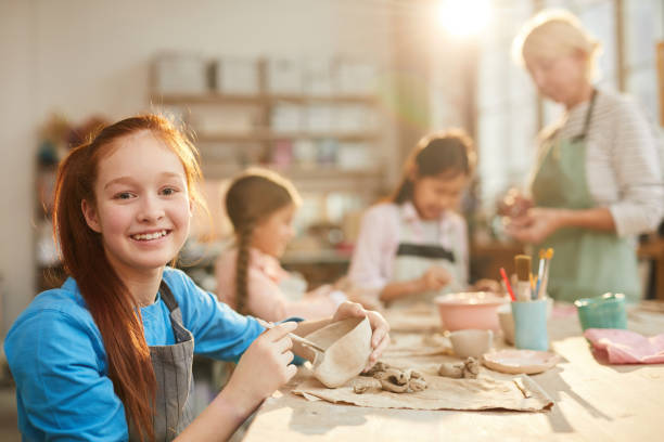 Teenage Girl in Pottery Studio Portrait of smiling teenage girl looking at camera while enjoying pottery class with group of children, copy space art class photos stock pictures, royalty-free photos & images