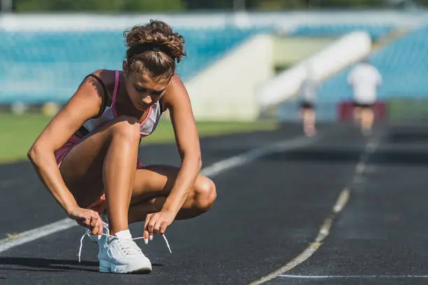 Close up of a young sportsgirl dressed in sportswear tying her shoelaces at the stadium.