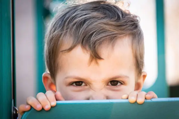 very upset three years old boy looking at the camera peeking at a playground