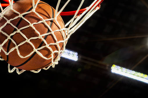 Looking up at the bottom of a basketball falling through the net with arena lights in the background